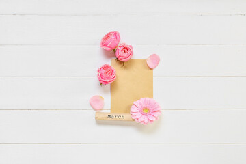 Composition with blank card, word MARCH and flowers on light wooden background. International Women's Day celebration