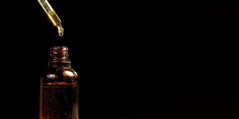 Cannabidiol oil in a small amber bottle on the black background, close-up shot. Dripping CBD oil drops, using a dropper.