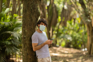 View of young man using a smartphone at day time with a green park in the background. High quality photo