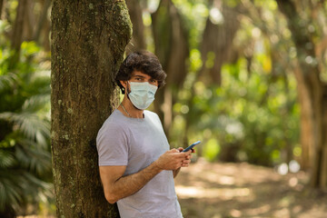 View of young man using a smartphone at day time with a green park in the background. High quality photo