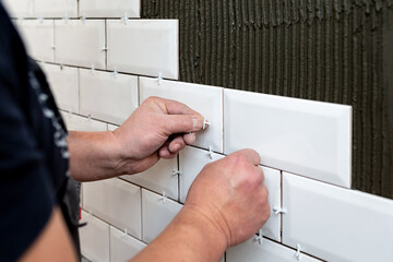 Workers hands install tile spacer between ceramic tiles. Stage of facing kitchen wall with white ceramic tiles. Construction details, repair work