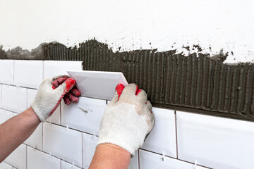Wall cladding. Workers hands installing ceramic tiles on kitchen wall. Construction details, repair...
