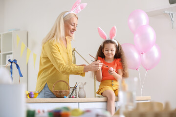 Little girl and her grandmother painting Easter eggs at home