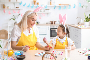Little girl and her grandmother painting Easter eggs at home
