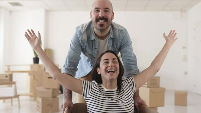 Happy couple having fun while unpacking on moving day in new apartment - First day at new house of funny man and woman - Moving and relocation concept. High quality 4k footage