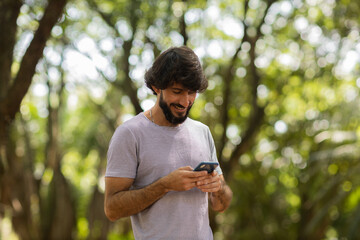 View of young man using a smartphone at day time with a green park in the background. High quality photo