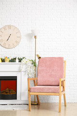 Pink armchair, lamp and fireplace near white brick wall