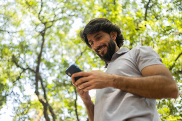 Fototapeta premium View of young man using a smartphone at day time with a green park in the background. High quality photo