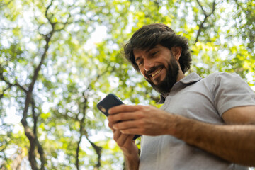 View of young man using a smartphone at day time with a green park in the background. High quality photo