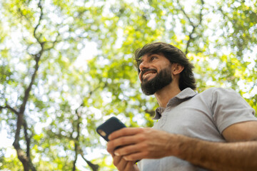 View of young man using a smartphone at day time with a green park in the background. High quality photo