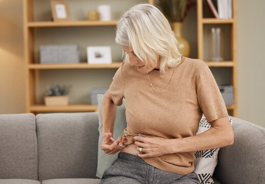 A shot a day keeps diabetes away. Shot of a mature woman injecting herself with insulin on the sofa at home.