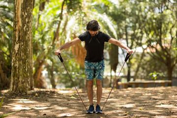 Strong man guy working out with elastic rubber bands at a park outdoors. Athlete male person during workout with additional sport equipment. High quality photo