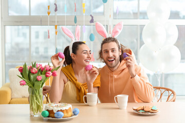 Happy couple in bunny ears with Easter eggs sitting at table