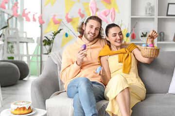 Young couple with basket and Easter eggs sitting on sofa at home