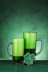 Glasses of beer and gingerbread cookie for St. Patrick's Day celebration on green background