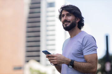 View of young man using a smartphone at day time with city view landscape in the background. High quality photo
