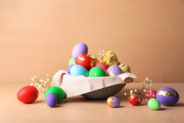 Bowl with beautiful Easter eggs and flowers on beige background