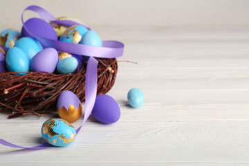 Nest with beautiful Easter eggs on light wooden table, closeup
