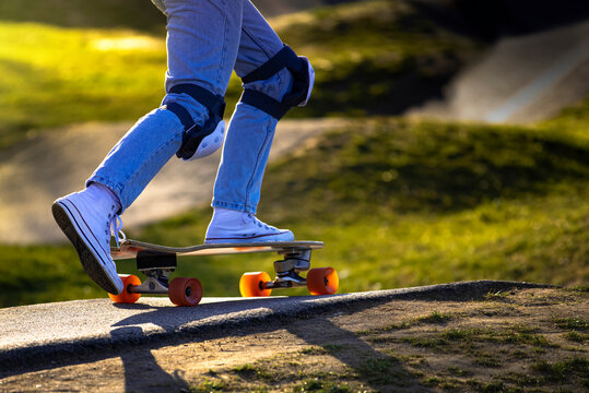 Legs of a girl in blue jeans and knee pads ride a skateboard in a skate park