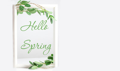 Spring background - a spring composition of green branches and the inscription Hello Spring on a white background. Copy space. Frame