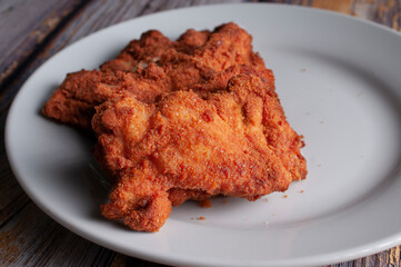 Breaded chicken on a white plate on an old wooden table, horizontal macro photography. Concept of crispy food, empty space on the side