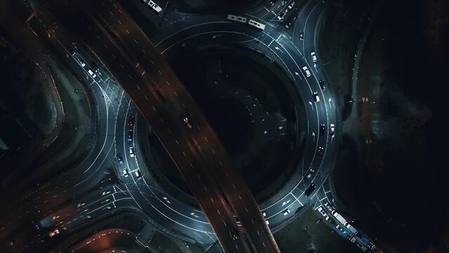 Aerial flyover car traffic roundabout interchange road at night, drone shot top down view expressway intersection in modern city in evening. Cars driving busy junction highway transportation