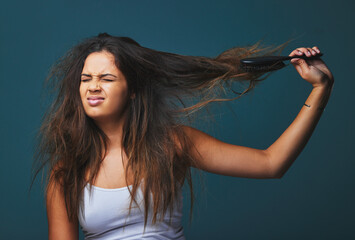 Nip, snip, girl, get a grip. Studio shot of a beautiful young woman pulling on her hair posing against a blue background.