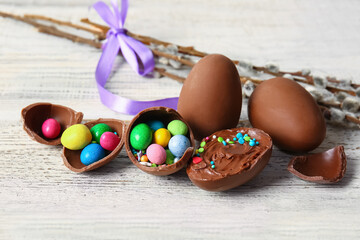 Broken chocolate Easter eggs with different candies on light wooden background
