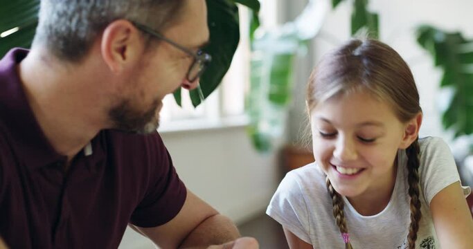 This dad makes the grade. Young father helping his little daughters study her homework. Cute, smiling girl child enjoying learning with her dad at home. Children education and home schooling concept