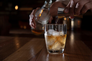 man hand pouring whiskey from jigger into glass