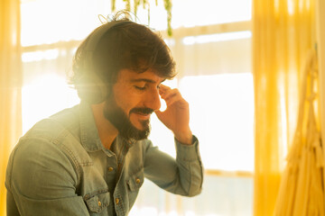 Fototapeta premium View of young man listening to music with headphones in his ears in the living room of his apartment. High quality photo.
