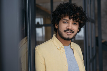 Young smiling Indian man looking at camera standing in modern office. Portrait of handsome...