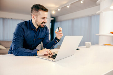 A man using his credit card for online shopping on the laptop from his cozy home.