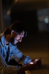 Side view of young man using a smartphone at night time with city view landscape in the background. High quality photo