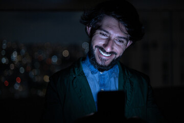 Front view of young man using a smartphone at night time with city view landscape in the background. High quality photo