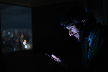Side view of young man using a smartphone at night time with city view landscape in the background. High quality photo