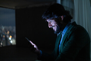Side view of young man using a smartphone at night time with city view landscape in the background. High quality photo