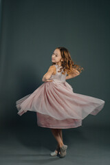 Photo in motion, a beautiful little girl in a fluffy soft pink dress is spinning on a plain gray...