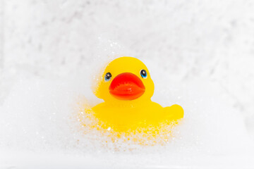 Yellow cheerful toy rubber duck in bath foam. Baby spa concept. Kids bath time