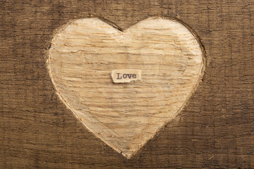 LOVE - tiny typed text note close up. Valentines Day greetings concept. Carved heart shape on wood as background for Valentines greeting card.