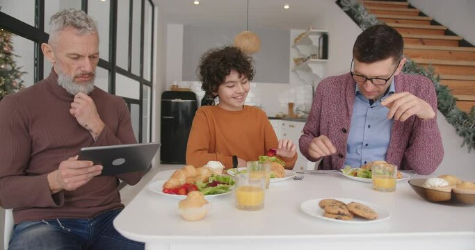 Gay man checks mail in tablet enjoying breakfast with family