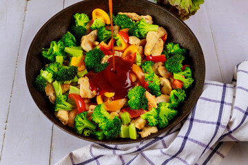 Spicy chicken with broccoli in pan on white background.