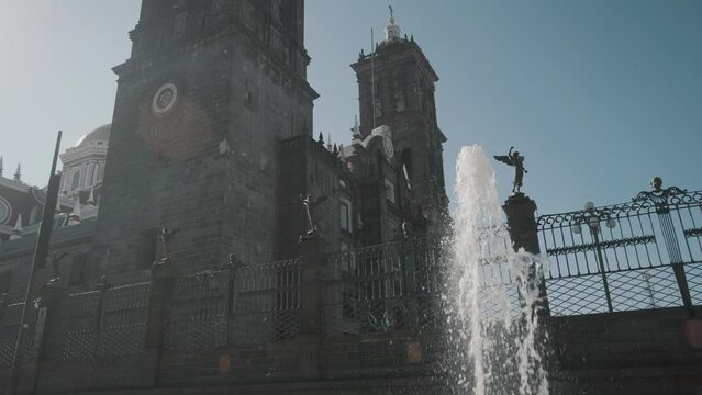 Slow motion shot of spraying fountain in front of Famous historic Cathedral against blue sky - Puebla,Mexico