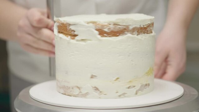 Chef's hands decorating rotating cake of four layers using pastry knife. Bakery process and confectionery making in slow motion.
