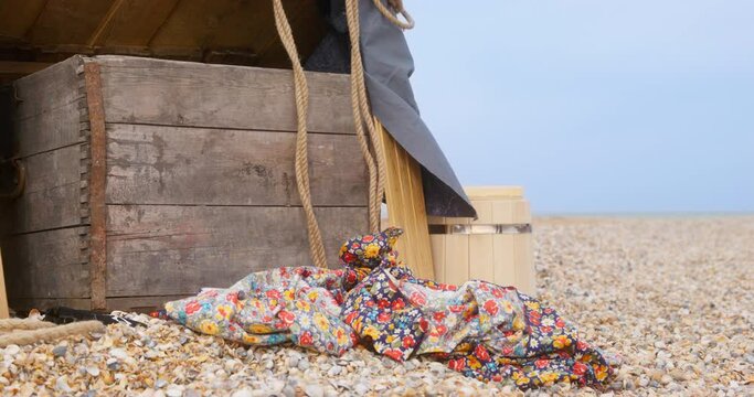 Black dachshund dog dressed as pirate with cocked hat runs past ship stuff and old patterned rag lying ON sea sand beach on cloudy day