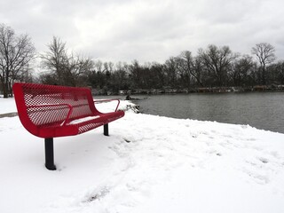 Snow-covered ground with a red bench by the lakeside in winter