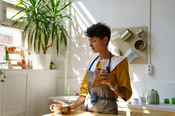 Young creative artisan crafts woman wearing apron drinking morning coffee from handmade clay mug...