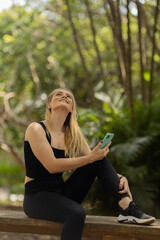 Young woman using a smartphone at day time with a green park in the background. High quality photo