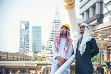 Fototapeta na wymiar Arab civil engineer construction project hold blueprint, pointing at construction site modern muslim UAE city. Multicultural diversity business people smart engineering intelligence. Engineer Concept.
