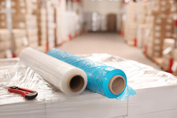 Rolls of different stretch wraps and utility knife on boxes in warehouse